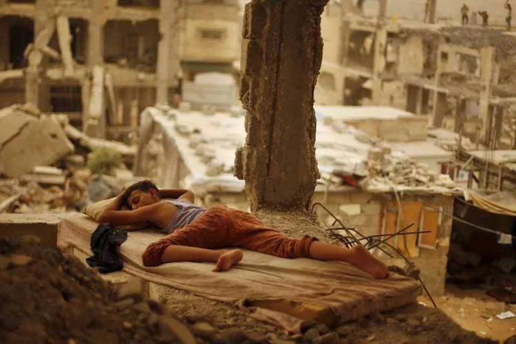 Menino palestino dorme em ruínas de casa durante tempestade de areia (REUTERS/Suhaib Salem)