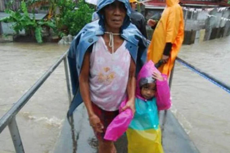Mulher com uma capa passa sobre um rio nas Filipinas devido à chegada do tufão, que  inundou muitas ruas e  deixou amplas áreas da capital sem energia elétrica  (Charism Sayat/AFP)