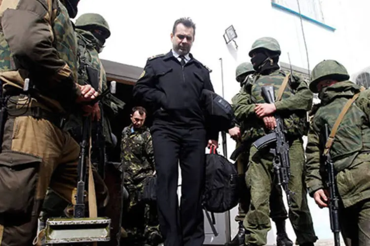Oficial naval ucraniano (c) passa por homens armados, possivelmente militares russos, a medida em que deixa o quartel naval em Sevastopol  (REUTERS/Vasily Fedosenko)