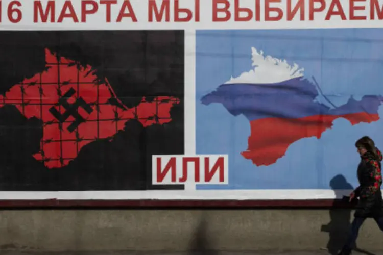 
	Em Sevastopol, na Crimeia, uma mulher passa em frente a um cartaz que compara a interfer&ecirc;ncia de Putin na regi&atilde;o ao expansionismo nazista
 (REUTERS/Baz Ratner)