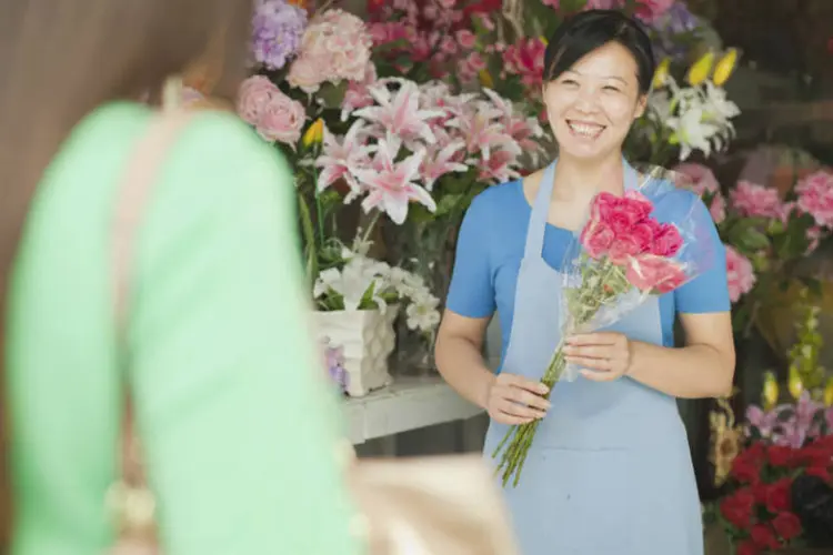 Vendedora com ramo de flores espera cliente em loja (floricultura) (XiXinXing/Thinkstock)