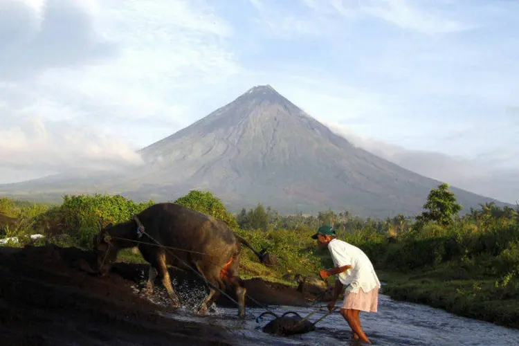 Fazendeiro anda com búfalo com o vulcão Mayon ao fundo, nas Filipinas (Stringer/Reuters)