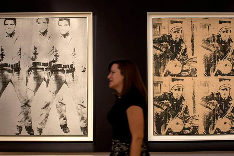 Mulher anda entre as obras "Triple Elvis" e "Four Marlons" de Andy Warhol na Christie's (REUTERS/Brendan McDermid)