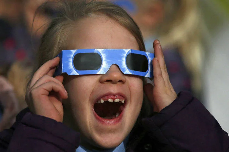 Criança com óculos protetores observa o eclipse na Inglaterra (Phil Noble/Reuters)
