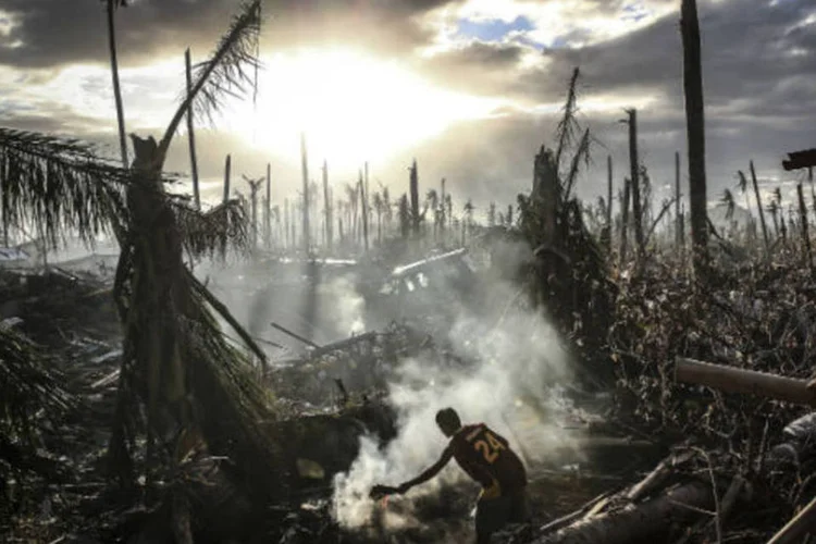 Um homem abana uma fogueira em meio a um cenário de destruição em Tanauan, nas Filipinas (Dan Kitwood/Getty Images)