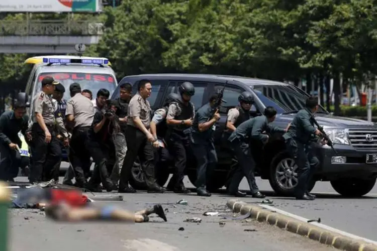 Cadáveres são vistos no chão enquanto a polícia indonésia aramada com rifles se proteje atrás de um carro em Jacarta (REUTERS/Beawiharta)