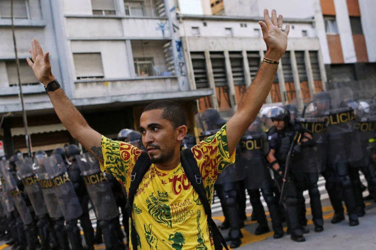 Manifestante levanta as mãos em frente a cordão policial (Nacho Doce/Reuters)
