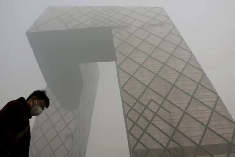 Homem de máscara passa em frente ao edifício China Central Television (CCTV) durante dia poluído em Pequim. (REUTERS)