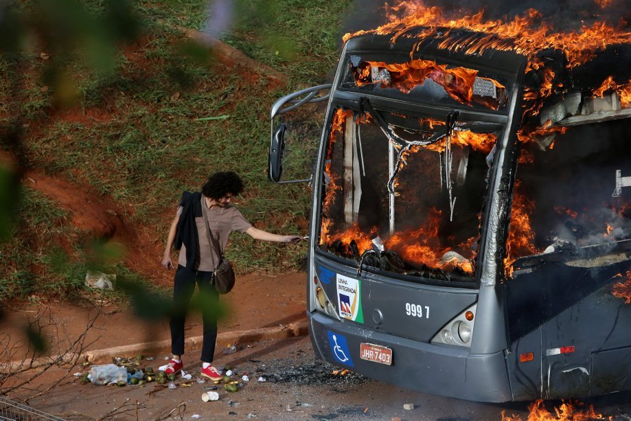 <span>Pessoa acende o cigarro em ônibus queimando durante protesto contra a PEC do teto dos gastos, em Brasília, dia 13/12/2016</span>