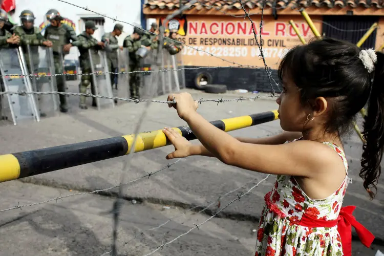 Foto de arquivo mostra uma menina parada em frente ao bloqueio de arame farpado e policiais na fronteira da Venezuela (Carlos Eduardo Ramirez/Reuters)