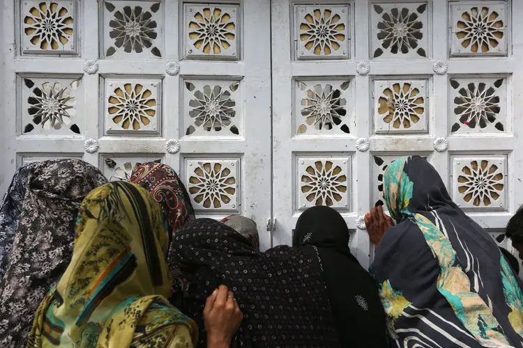 Mulheres aguardam do lado de fora de templo sufi para recuperarem seus pertences após ataque suicida (Akhtar Soomro/Reuters)