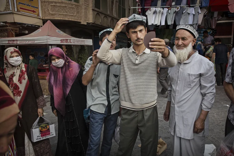 Jovem de minoria muçulmana uigure experimenta adereço tradicional em comércio de Xinjiang, na China (Kevin Frayer/Getty Images)