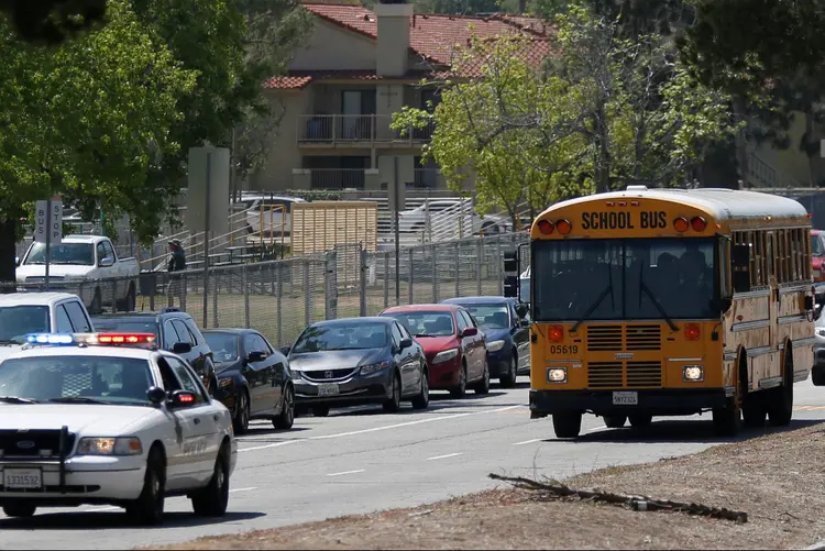 Carros de polícia escoltam alunos após tiroteio: o atirador foi identificado como Cedric Anderson, de 53 anos, de San Bernardino, e sua esposa foi identificada como Karen Elaine Smith (Mario Anzuoni/Reuters)