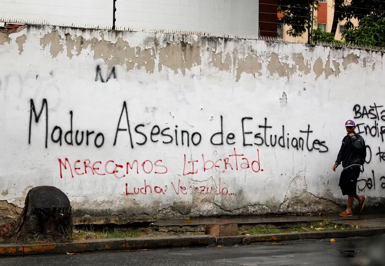 Homem caminha em frente a parede pichada com mensagem contra o governo: "Maduro assassino de estudantes", Caracas, Venezuela, dia 13/04/2017 (Christian Veron/Reuters)