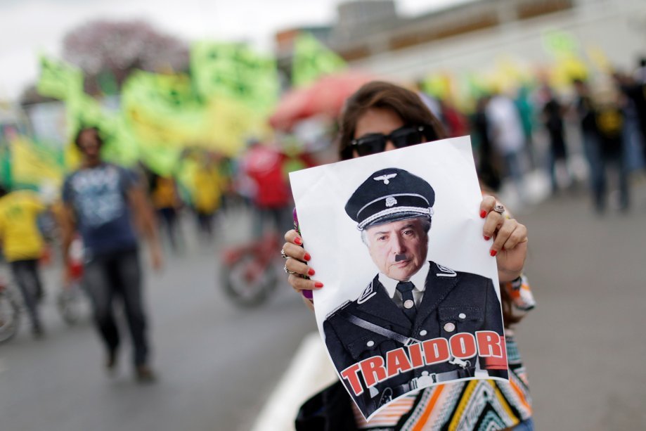 Mulher segura uma foto de Temer vestido de Hitler durante protesto no Congresso Nacional em Brasília na greve geral