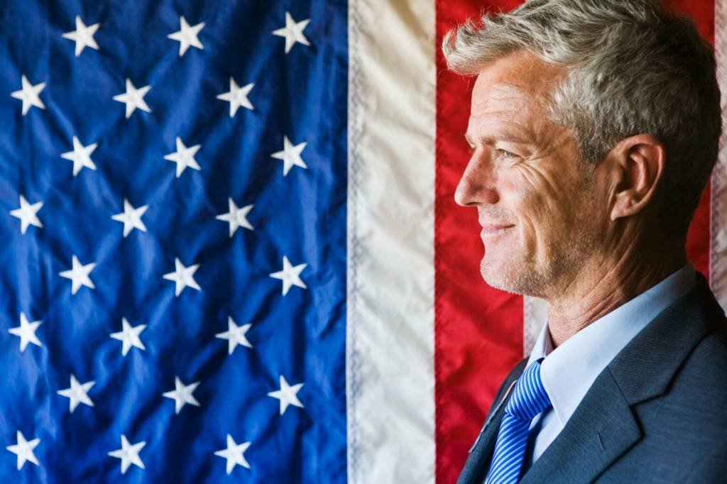Executivo norte-americano com bandeira dos Estados Unidos no fundo (Jupiterimages/Thinkstock)