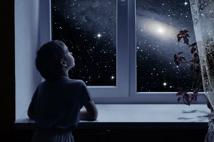 Menino olha para céu estrelado pela janela (Rastan/Thinkstock)