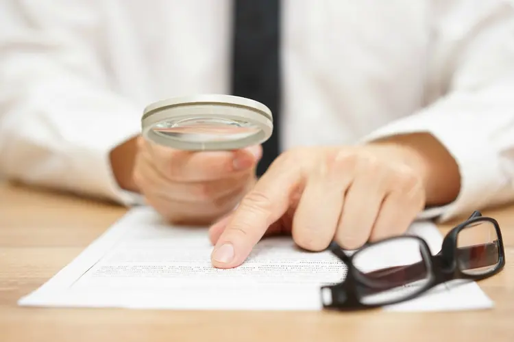 Focused businessman is reading through  magnifying glass document (BernardaSv)