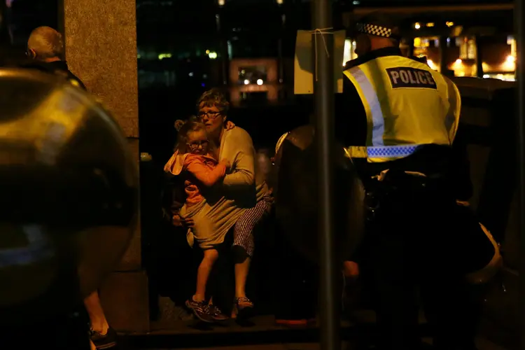 Pessoas se protegem enquanto a polícia chega ao local dos ataques na cidade (Neil Hall/Reuters)