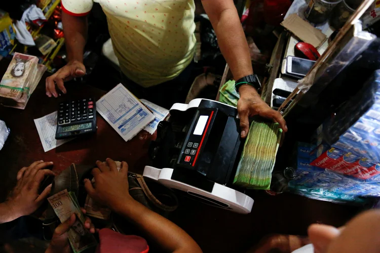 TRÁFICO DE COMIDA: Venezuelanos cruzam a fronteira para comprar alimento. Comerciante conta notas de bolívar no Porto Santander, na Colômbia / Carlos Garcia Rawlins/Reuters