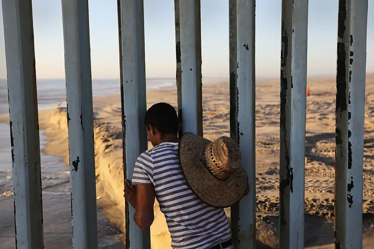 FRONTEIRA MÉXICO-EUA: homem olha através de cerca construída na cidade de Tijuana; local é usado para encontro entre mexicanos deportados e seus familiares que ficaram nos EUA / John Moore/ Getty Images (John Moore/Getty Images)