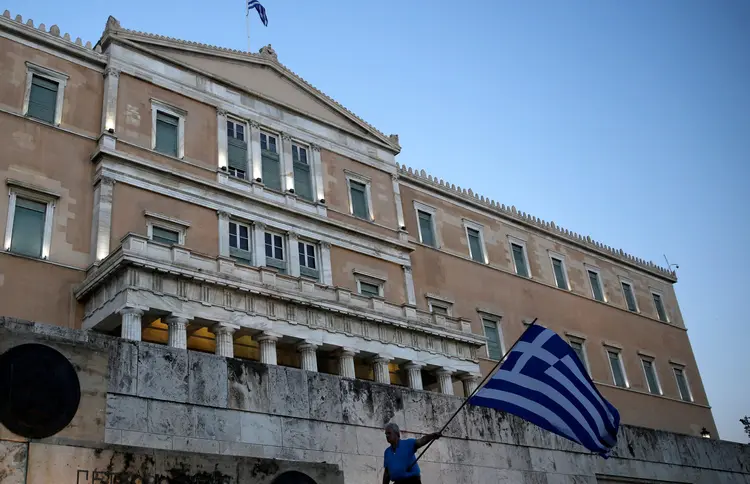 Homem segura bandeira da Grécia em frente ao parlamento grego em Atenas: país manteve grau de investimento (Costas Baltas/Reuters)
