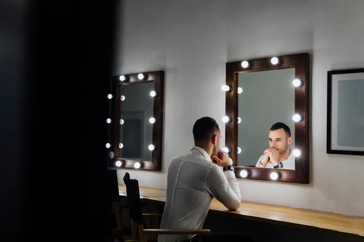 Portrait of handsome young man in white shirt looking into the mirror. Male reflection, light bulbs. (photominus/Thinkstock)