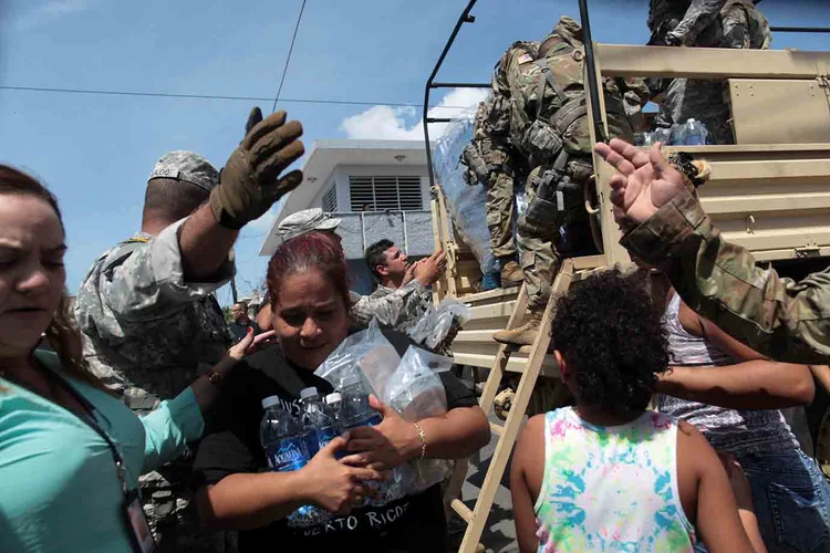 Mulher carrega garrafas de água e alimento durante distribuição de mantimentos em Porto Rico. (ALVIN BAEZ/Reuters)