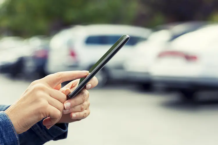 Mulher usando celular e carros: ferramentas são oferecidas por portais de classificados e também startups que realizam leilões online. (LDProd/Thinkstock)