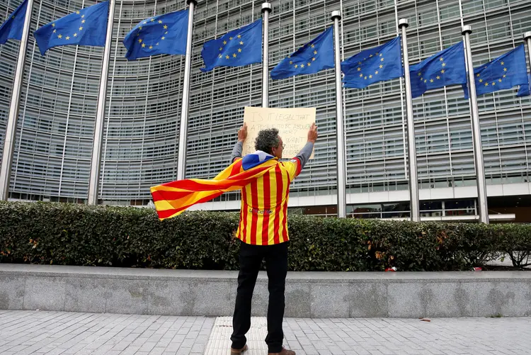 Homem vestido com a bandeira da Catalunha segura cartaz em frente a bandeiras da União Europeia (Francois Lenoir/Reuters)