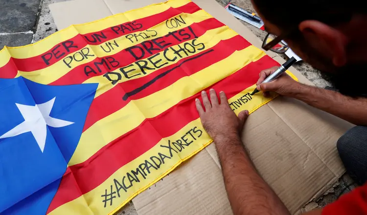 Homem escreve em bandeira separatista da Catalunha: "Por um país com direitos" (REUTERS/Yves Herman/Reuters)