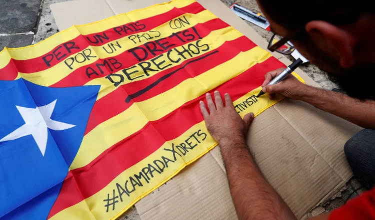 Homem escreve em bandeira separatista da Catalunha: "Por um país com direitos" (REUTERS/Yves Herman/Reuters)
