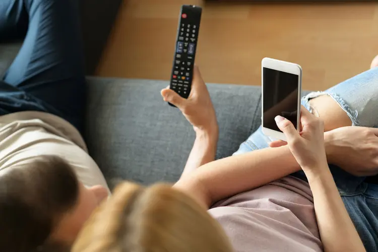 Mulher segura celular enquanto assiste à tv (AndreaObzerova/Thinkstock)