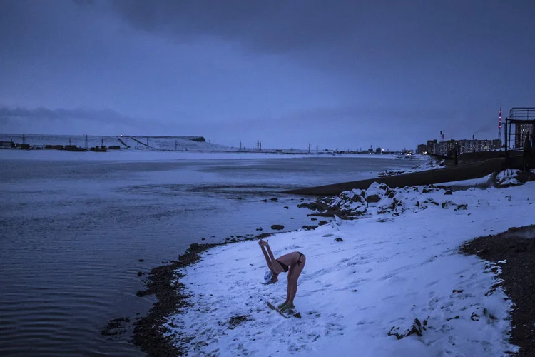 MULHER SE AQUECE NA BEIRA DO LAGO DOLGOYE, EM NORILSK: antes um campo de trabalho escravo, a cidade é a mais fria, poluída e mais rica cidade industrial da Rússia /  (Sergey Ponomarev/The New York Times)