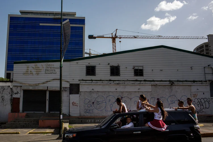 Pessoas em um carro passam na frente de uma clínica animal fechada e um prédio novo no bairro de Las Mercedes em Caracas, na Venezuela  (Manaure Quintero/Bloomberg)