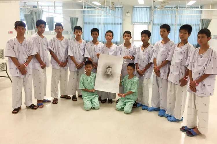 Os 12 membros do time de futebol da Thailândia e seu treinador posam ao lado de uma figura de Samarn Kunan, mergulhador voluntário que morreu durante o resgate, no hospital de Chiang Rai Prachanukroh  (Chiang Rai Prachanukroh Hospital AND Ministry of Public Health/Reuters)