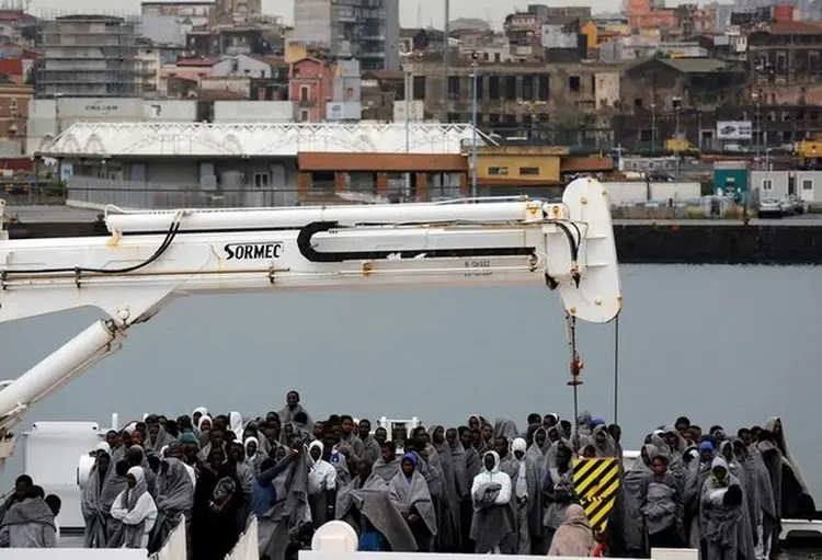 Imigrantes aguardam para desembarcar de embarcação da Guarda Costeira italiana em porto da Sicília: "Por uma acolhida digna dos refugiados em uma Europa sem fronteiras", afirmava um dos cartazes exibidos (Antonio Parrinello/Reuters)