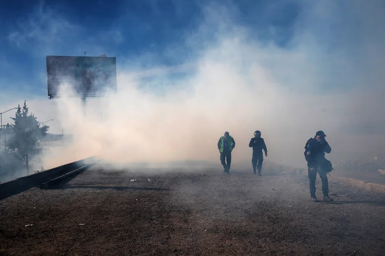 Caravana de imigrantes: Helicópteros de patrulha da fronteira dos EUA voaram baixo, enquanto agentes americanos realizaram uma vigília a pé além da cerca de arame (Adrees Latif/Reuters)