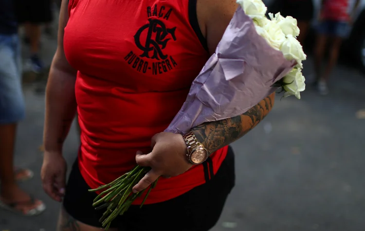 Mulher com flores brancas em enterro de jovem que morreu no incêndio no CT do Flamengo (Pilar Olivares/Reuters)