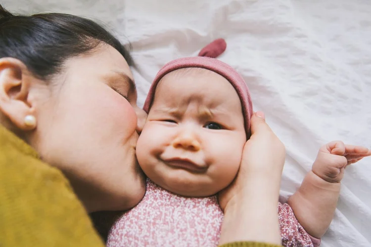 Mãe na cama junto com bebê fazendo careta (Tuan Tran/Getty Images)