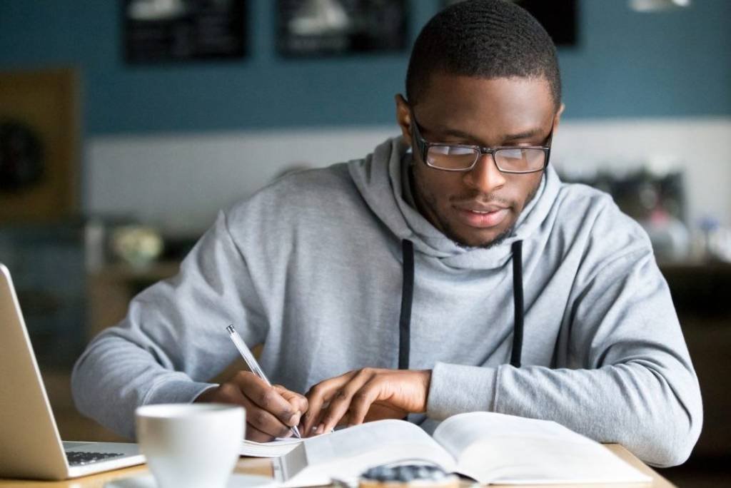 Homem concentrado estudando com livro e computador (fizkes/Getty Images)