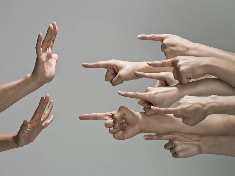 Multiple white hands are pointing index fingers from the right to the left at one set of hands.  The pair of hands that are being pointed at are up in a defensive pose, with fingers to the sky and palms towards the pointing fingers. (foto/Getty Images)