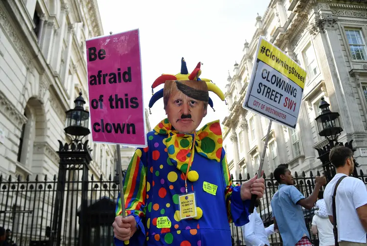 An anti-Brexit protester wearing a clown costume and a defaced mask depicting British Prime Minister Boris Johnson holds placards in Westminster in London, Britain August 29, 2019. REUTERS/Toby Melville (Toby Melville/Reuters)