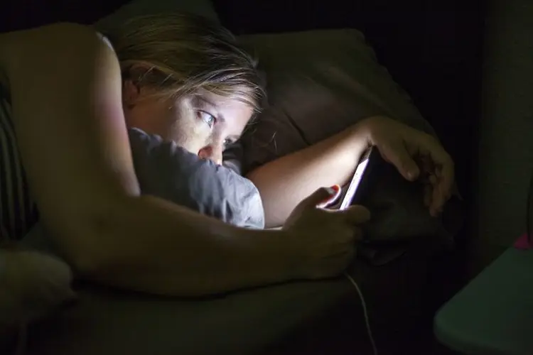 Caucasian woman using cell phone in bed (Adam Hester/Getty Images)