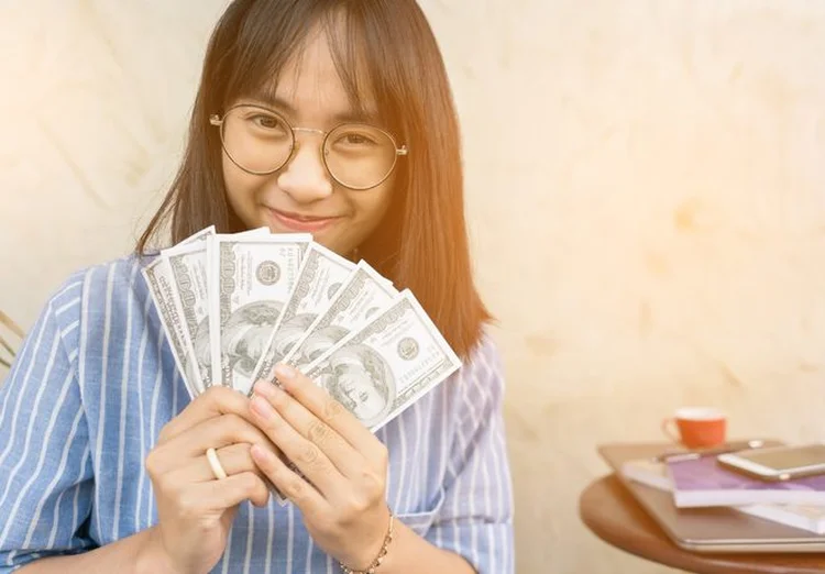 Jovem sorrindo e segurando dinheiro
 (Jidpipat Taewiriyakun / EyeEm/Getty Images)