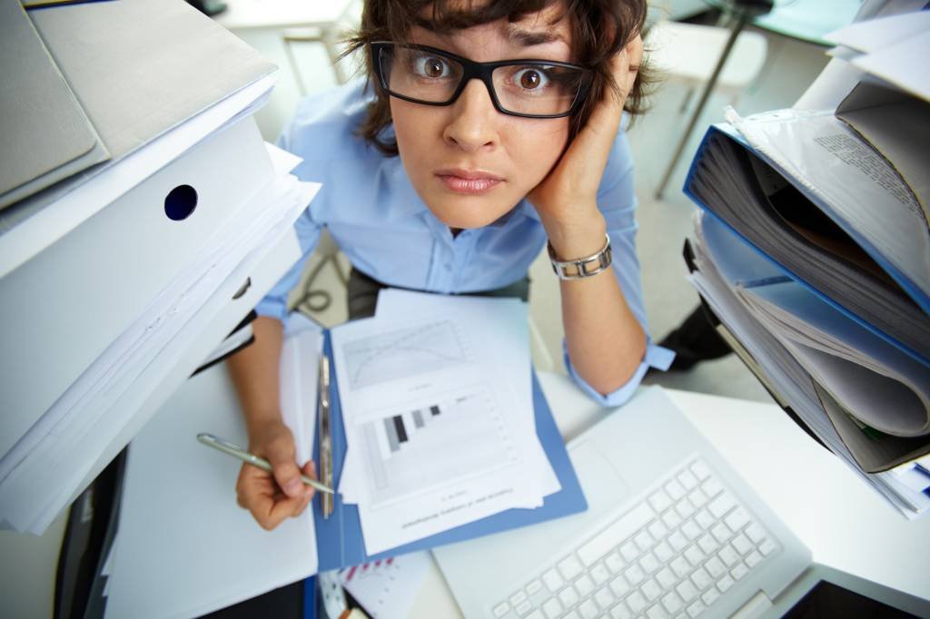 Perplexed accountant doing financial reports surrounded by huge piles of documents (Designed by Pressfoto / Freepik.com/Creative Commons)