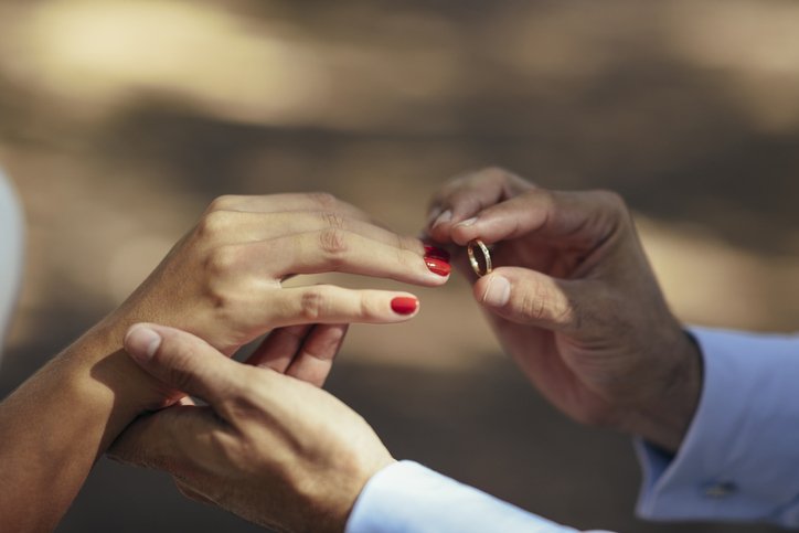 Groom putting wedding ring on finger of bride, close up