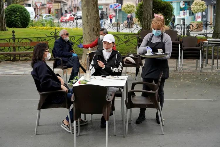 Garçonete com máscara de proteção serve clientes em Cuenca, na Espanha (Juan Medina/Reuters)