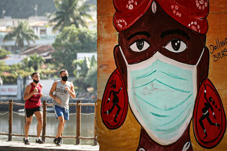 Homens correm perto de grafite representando mulher usando máscara protetora, após o surto de coronavírus. Rio de Janeiro, 8 de junho de 2020. (Sergio Moraes/Reuters)