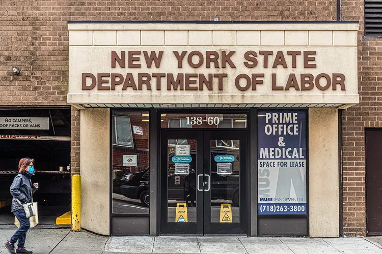 Pedestre usando máscara de proteção passa pelo prédio do Departamento de Trabalho do Estado de Nova York, no bairro de Queens, em Nova York, EUA, na terça-feira, 14 de abril de 2020.  (Jeenah Moon/Bloomberg)